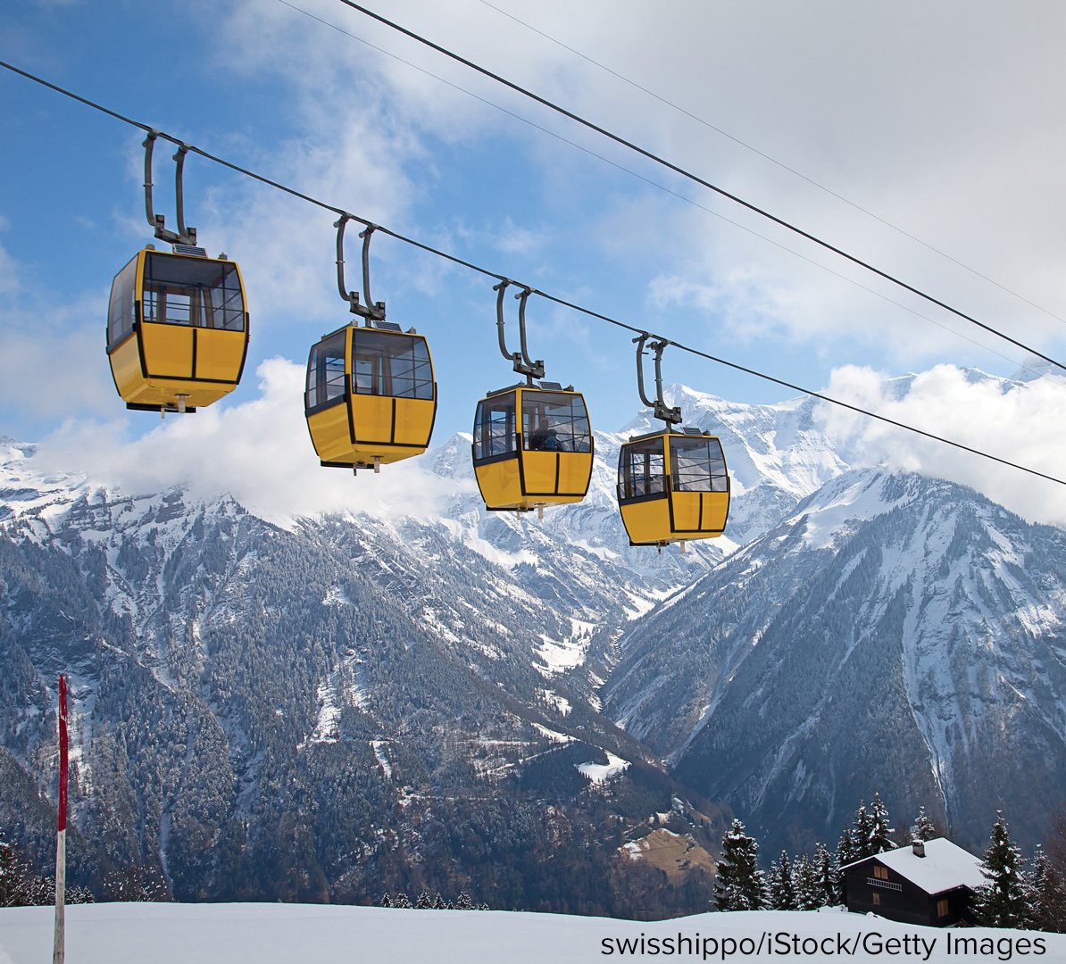 Yellow gondola cabins hanging from a cable, crossing a snow-covered mountain valley.