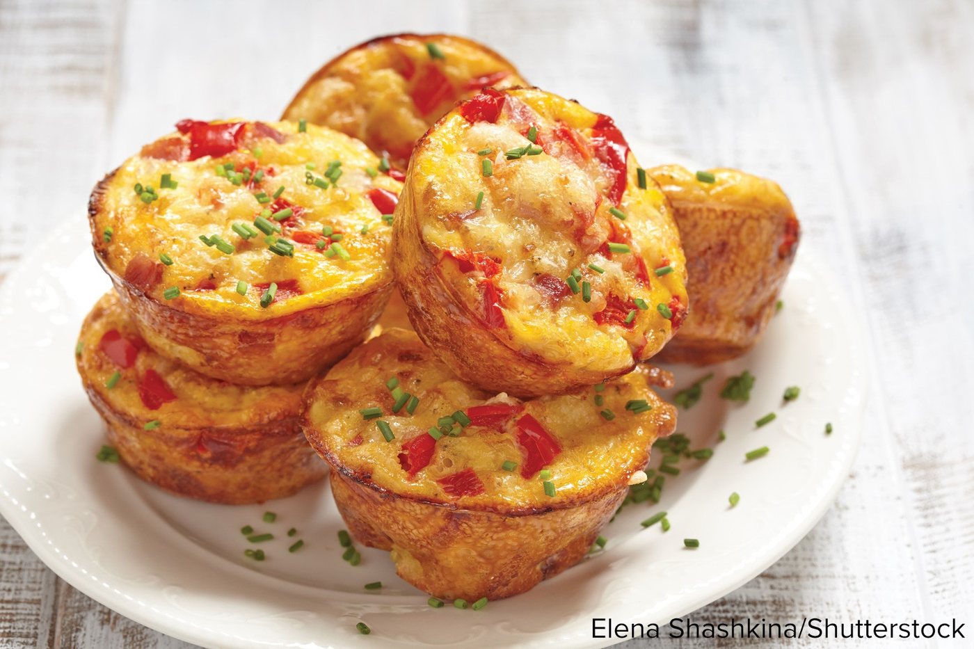 A white plate stacked with baked egg muffins, sprinkled with chives.