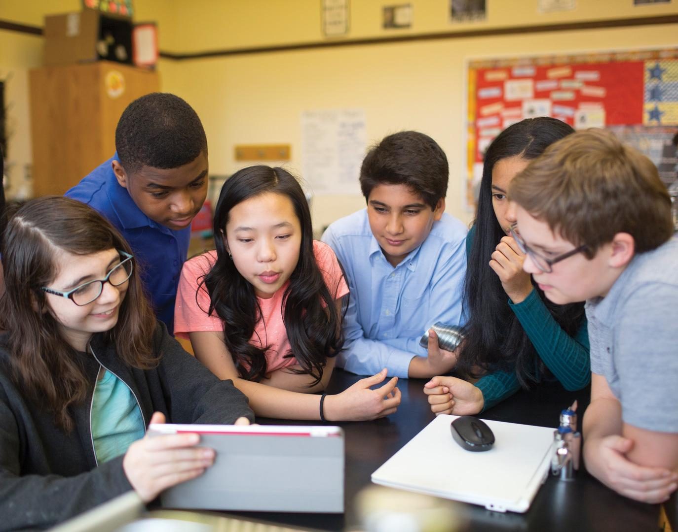 A group of students leaning in together around a tablet, working out a problem as a team.