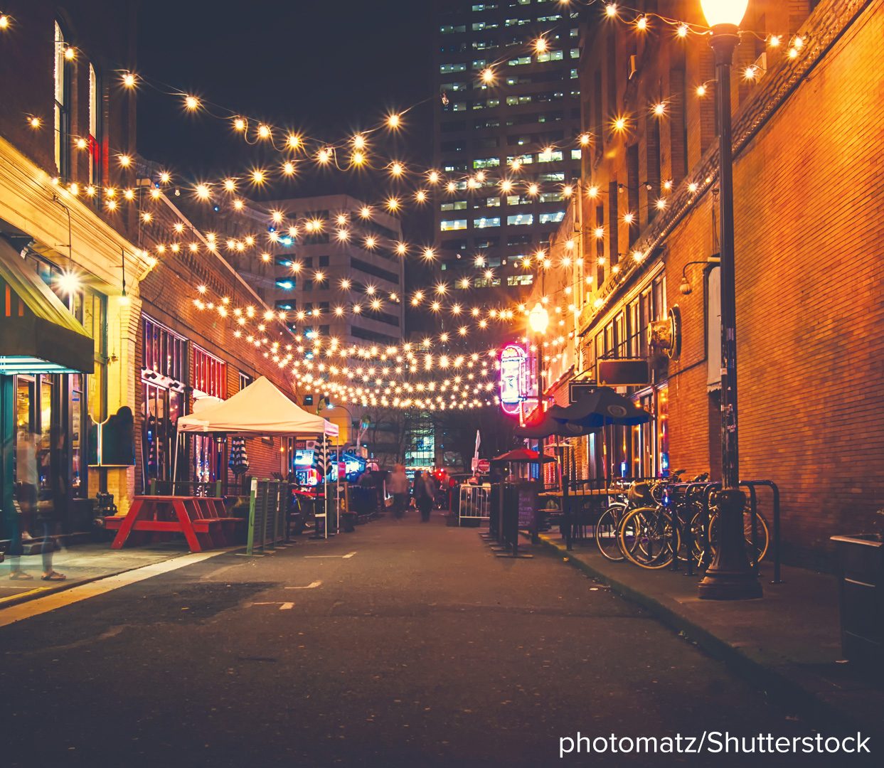 A city street at dusk strung with rows of hanging lights receding into the distance.