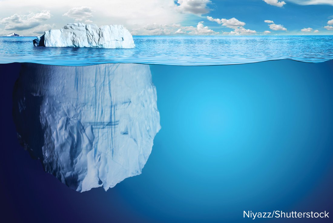 A photograph of an iceberg, with a small part above the waterline and a much larger mass below.