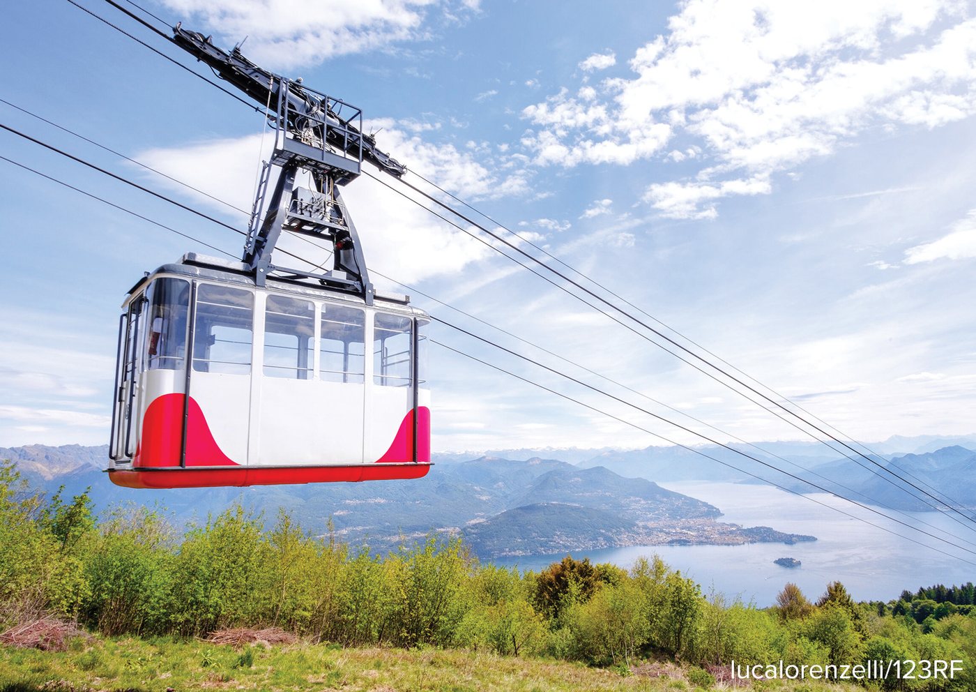 A cable car suspended on a wire, travelling above a lake and green hillside.