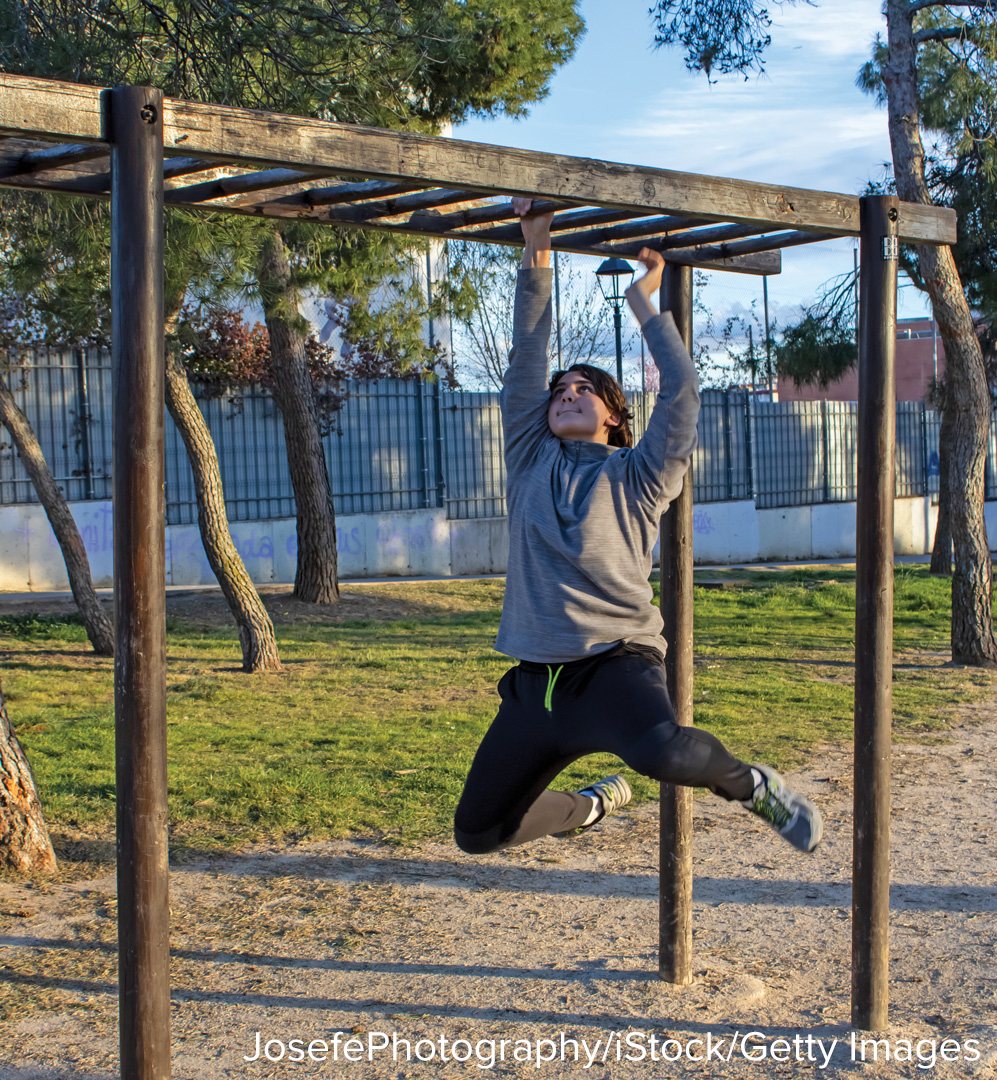 A student swinging hand over hand along a set of monkey bars in a playground.